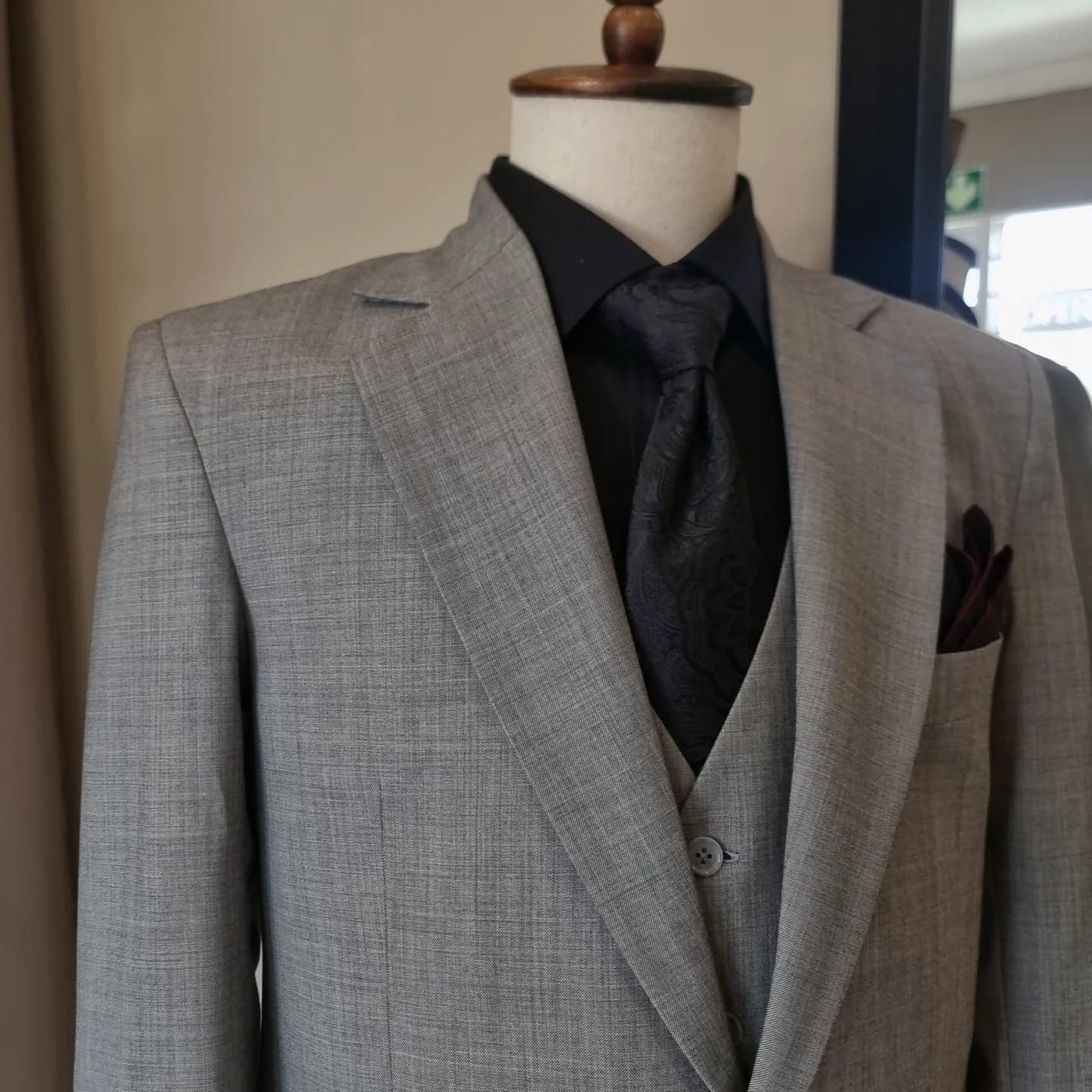 A grey check three-piece suit with a black shirt and tie