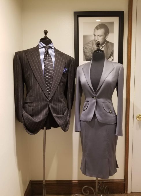 A grey ladies skirt suit beside a men's pinstripe suit in the studio