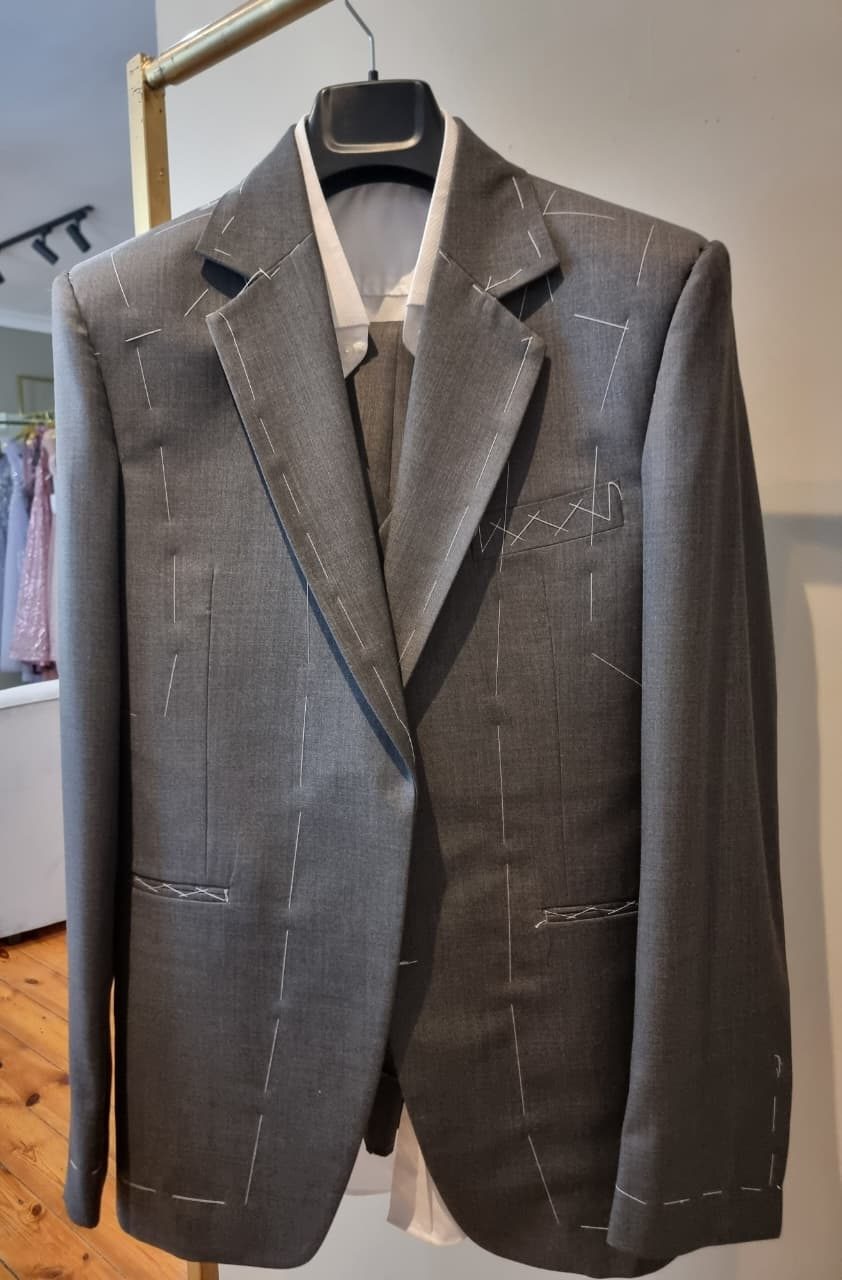 A grey jacket at the baste fitting, marked with white tacking thread